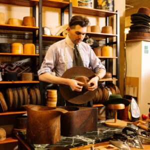 A young man at a desk inspects a hat