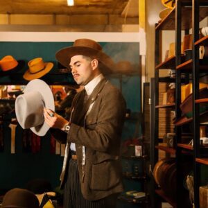 A young man in period dress brushes down a felt hat